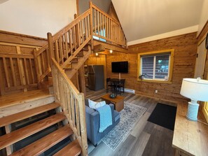 A wooden interior with a staircase, a flat-screen TV, a dining area, and a window.