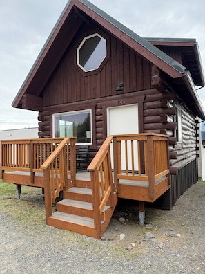 A log cabin with a wooden deck, a large window, and a garage.
