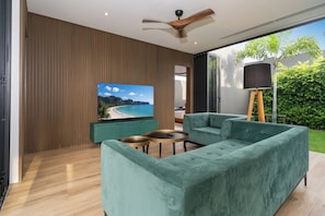 Uma sala de estar moderna com uma grande TV de tela plana, sofás verde-água e um ventilador de teto.