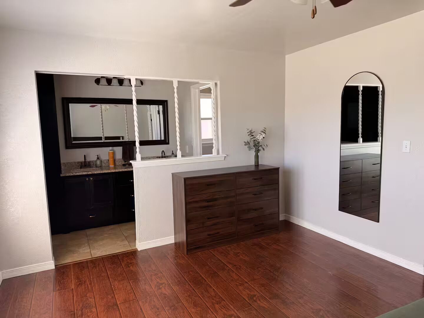 A bathroom with a dark wood vanity, a large mirror, and a window.