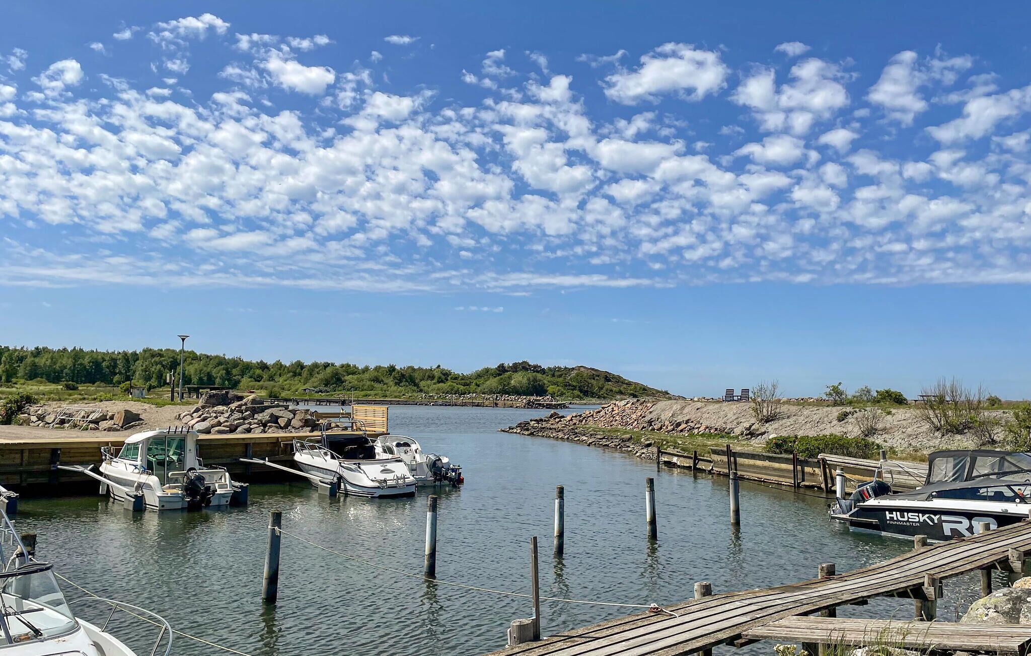 Un port de plaisance avec des bateaux amarrés, une jetée en bois et, au loin, un paysage vallonné.