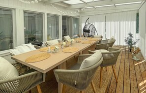 Un espace repas avec une longue table en bois, des chaises en osier et un fauteuil suspendu.