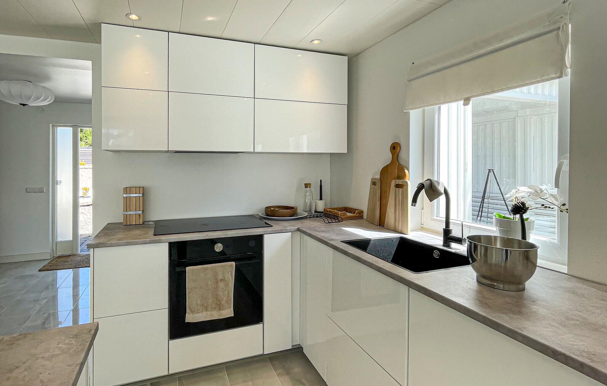 Une cuisine moderne avec des meubles blancs, un four noir, un évier en acier inoxydable et une fenêtre donnant sur un beau paysage.