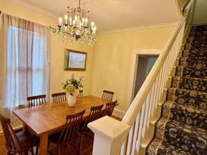 Comedor con mesa de madera, sillas, una lámpara de araña y una escalera con alfombra estampada.