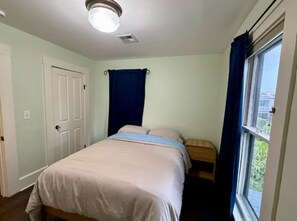 A bedroom with a bed, a window with curtains, a door, and a ceiling light fixture. - Large home in perfect Eugene location! (Eugene)