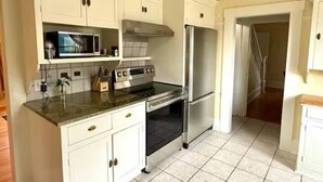 Una cucina con mobili bianchi, un frigorifero in acciaio inox, un forno a microonde e un piano cottura.