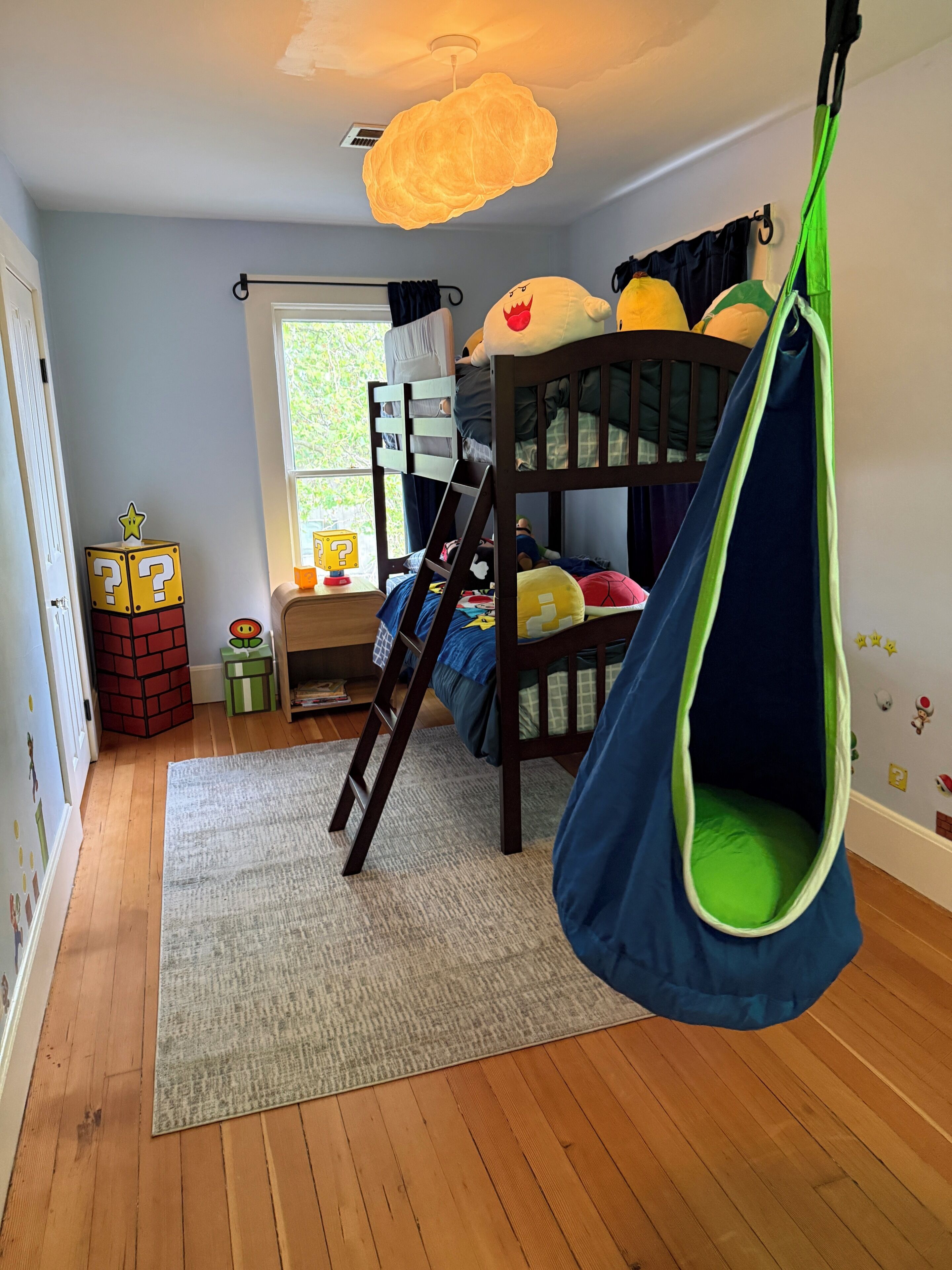 Ein Kinderzimmer mit Etagenbetten, einem Hängekorbsessel, einem Fenster und einer Tür.