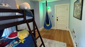 Un letto a castello con una scala, una sedia sospesa, una porta e un muro con adesivi.