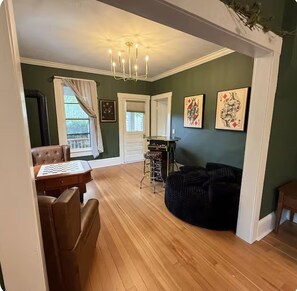 A room with a wooden floor, a dining table with chairs, a black bean bag, a chandelier, and artwork on the walls. - Do not book, not available. Can’t get VrBO to help remove listing (Eugene)