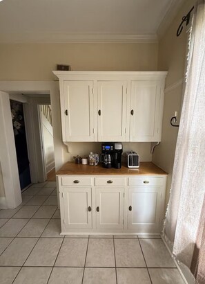 Una cocina con armarios blancos, encimera de madera y cafetera.