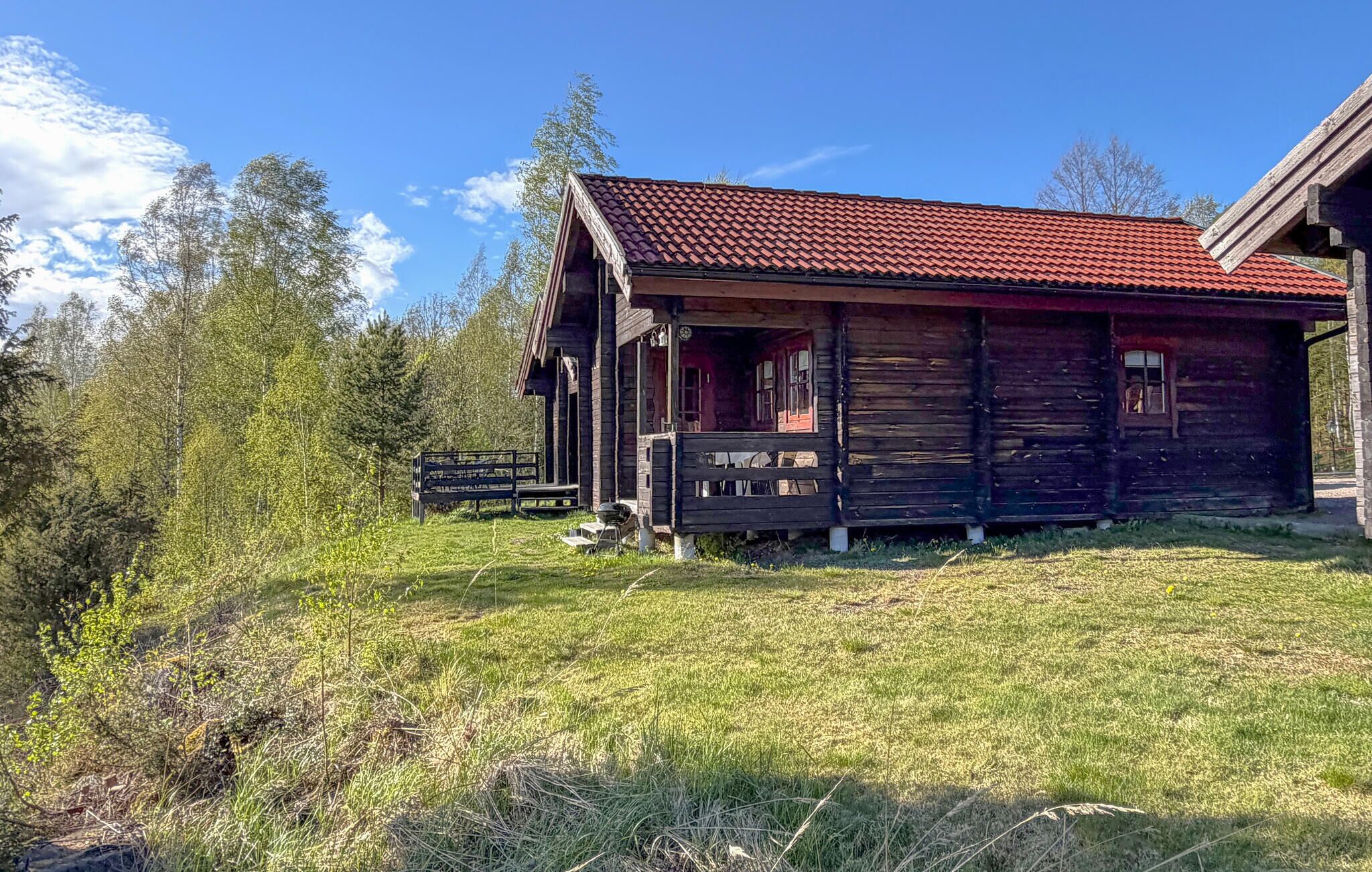 A rustic wooden cabin with a red-tiled roof, surrounded by a grassy field and trees.