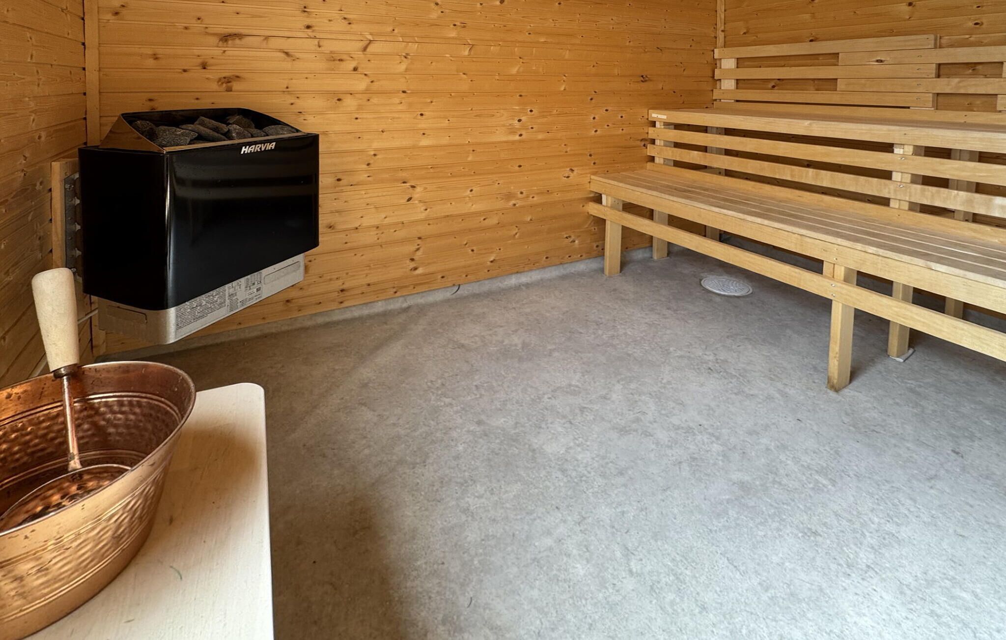 A sauna room with a Harvia sauna, wooden benches, and a copper basin.