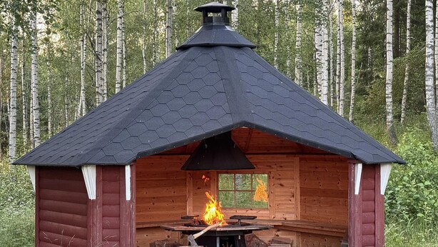 A wooden cabin with a hexagonal roof, a central fire pit, and a window. - Cozy home in årjäng with sauna (Årjäng)