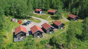 A cluster of wooden cabins with red roofs, surrounded by dense forest, and a gravel parking area with vehicles. - Cozy home in årjäng with sauna (Årjäng)