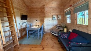 A wooden cabin interior with a dining table, chairs, a sofa, a ladder, a television, and framed pictures on the walls. - Cozy home in årjäng with sauna (Årjäng)