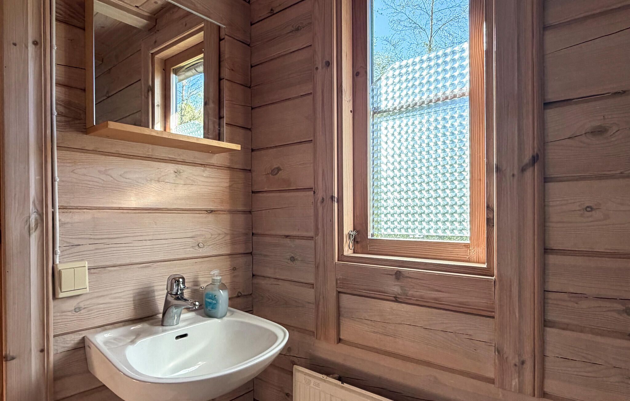 Baño de cabaña de madera con lavabo blanco, un espejo y una ventana.
