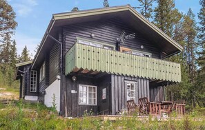 A wooden house with a balcony, a porch with wooden furniture, and a sign indicating a room number.