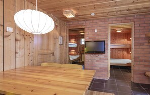 A wooden interior with a dining table, bunk beds, and a television.