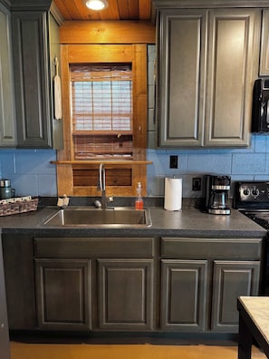 A kitchen with a granite countertop, stainless steel sink, wooden cabinets, a built-in oven, and a coffee maker. - Charming Waterfront Cabin on Lake Travis (Leander)