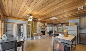 A spacious kitchen with a stone fireplace, wooden ceiling, and a dining area with a table and chairs. - Charming Waterfront Cabin on Lake Travis (Leander)
