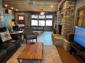 A cozy living room with a stone fireplace, a leather sofa, a wooden coffee table, and a television. - Charming Waterfront Cabin on Lake Travis (Leander)