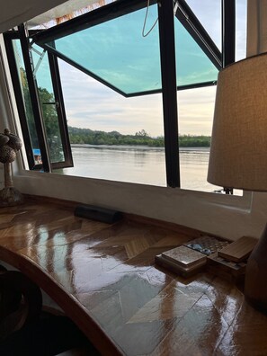 A room with a large window overlooking a river, a wooden desk, and a lamp. - Coconest ONE: Floating Couple Unit Waterstay on a UNESCO Site (Langkawi)