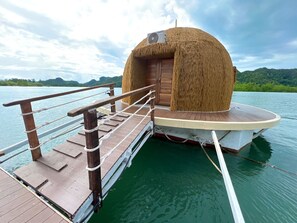 A boat with a thatched structure, a wooden deck, and a rope railing.