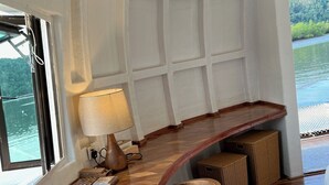 Una habitación con un banco de madera curvo, una lámpara, cestas de mimbre y vistas a una masa de agua a través de amplios ventanales.