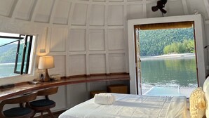 Una habitación con cama, escritorio, silla, lámpara y vista a un lago.