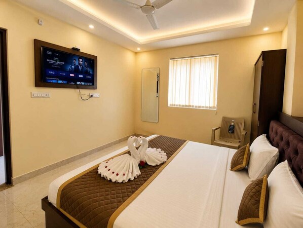 A hotel room with a bed, a television mounted on the wall, a window with curtains, and a ceiling fan. - Hotel Sunny (Udaypur)