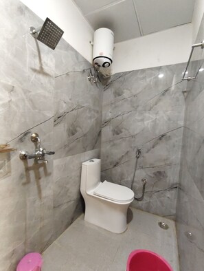 A bathroom with a toilet, shower, and a toilet paper holder. - Hotel Sunny  (Udaypur)