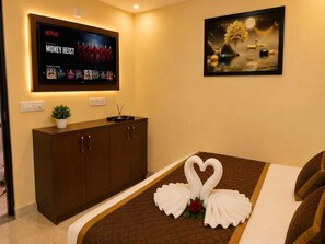 A hotel room with a bed, a TV displaying a Netflix series, a painting, and a cabinet with a plant. - Hotel Sunny (Udaypur)