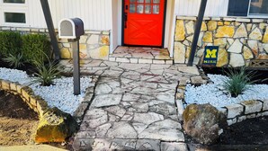 A house with a red door, stone steps, a mailbox, and a stone wall with a 'M' sign. - Welcome to The Royal Ranch: Your Ultimate Retreat in Central Dallas! (Dallas)