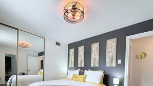 A bedroom with a large bed, a bedside table with a lamp, a mirror, and artwork on the wall. - Welcome to The Royal Ranch: Your Ultimate Retreat in Central Dallas! (Dallas)
