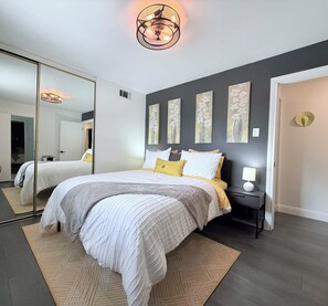 Ein Schlafzimmer mit einem großen Bett, einem Nachttisch mit Lampe, einem Spiegel und Bildern an der Wand.