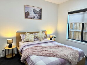 Een slaapkamer met een bed, twee bedlampjes, een nachtkastje, een foto aan de muur en een raam met uitzicht.
