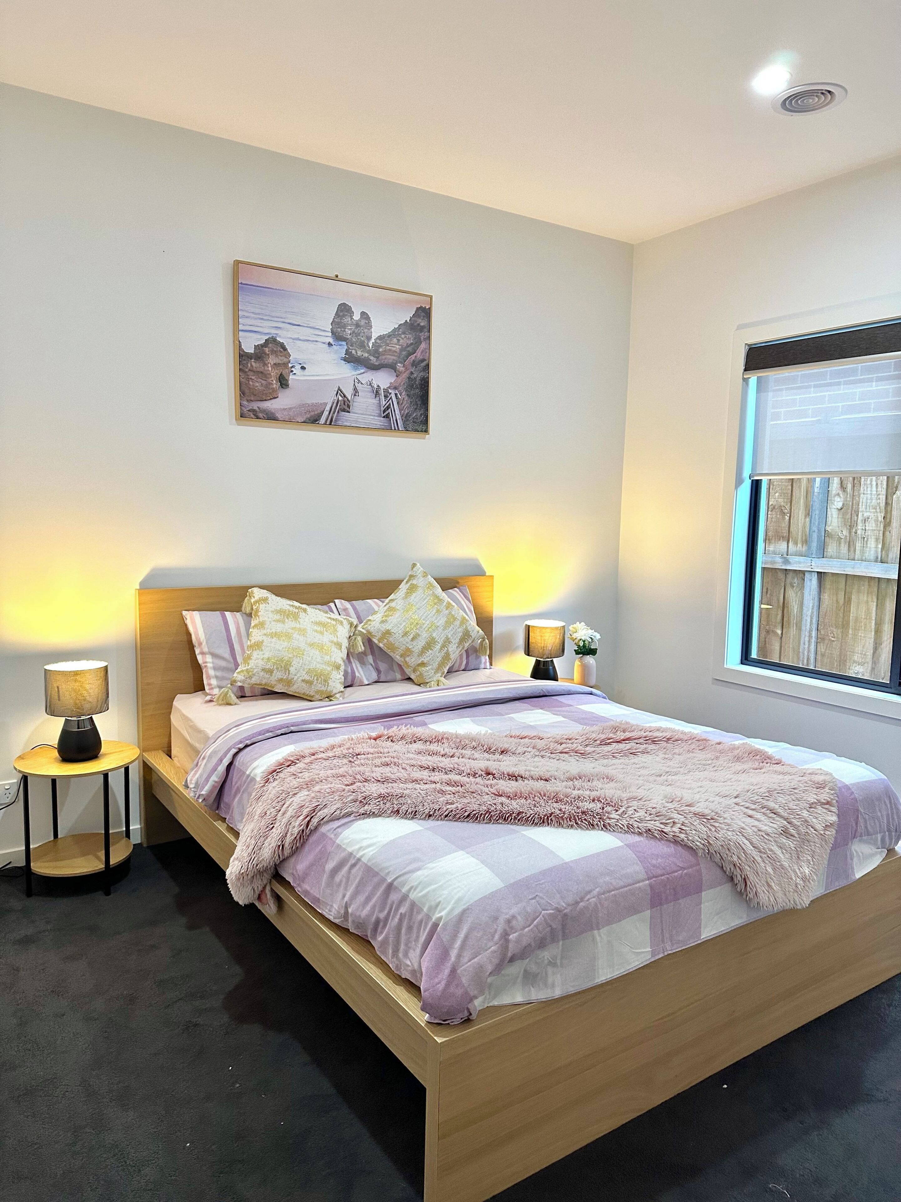 A bedroom with a bed, two bedside lamps, a window, and a picture on the wall.