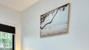 A bedroom with a bed, a window, a plant, and a painting on the wall.