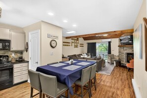 A kitchen with a stove, microwave, and cabinets, a dining area with a table and chairs, a living room with a sofa and fireplace, and a sign that reads 'SKI GAMELBOUR'. - Camelback Family Escape | Ski-In/Out + Game Room (Tannersville)