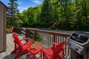 A deck with red chairs, a grill, and a bottle of wine. - Camelback Family Escape | Ski-In/Out + Game Room (Tannersville)