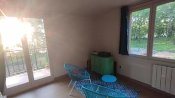 Ein Zimmer mit einem großen Fenster, einer grünen Kommode, zwei blauen Stühlen und einem gemusterten Teppich.