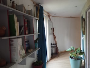 Een kamer met een boekenkast, een kamerplant, een houten ladder en een raam met gordijnen.
