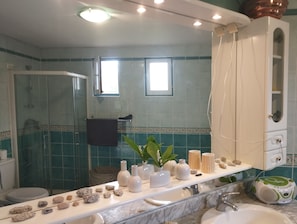 Casa de banho com chuveiro, pia, espelho e toucador com um porta-toalhas.