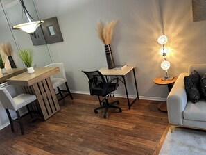 Een moderne woonkamer met een houten eettafel, een zwarte bureaustoel, een grijze bank en een decoratieve lamp.