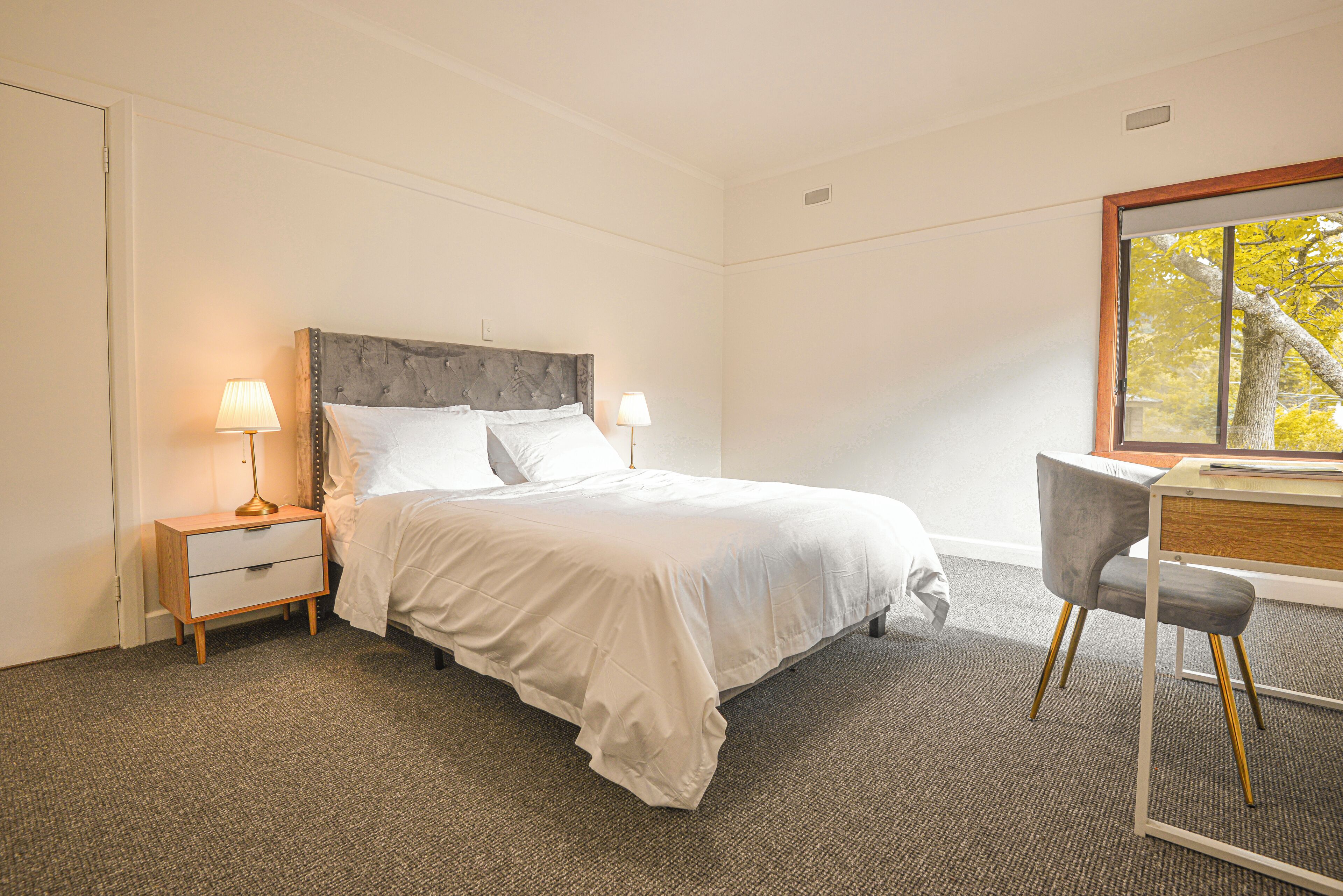 A bedroom with a bed, bedside tables, a desk, and a chair.