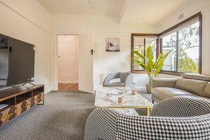 Een moderne woonkamer met een televisie, bank, salontafel en een groot raam.