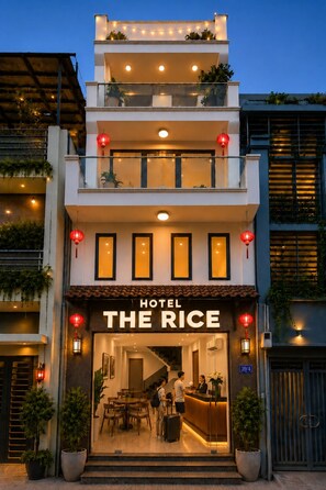 Ett hotell som heter ”Hotel The Rice” med en modern fasad, en reception och en trappa som leder upp till de övre våningarna.