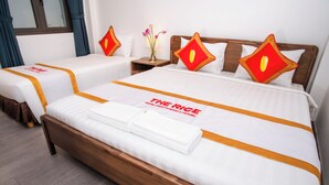 Habitación de hotel con dos camas, cada una con cubrecama blanco y detalles naranja. Se aprecia un cabecero de madera, una mesita de noche con un florero y una ventana con cortinas.