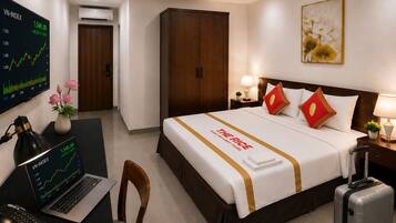 A hotel room with a bed, a desk with a laptop, a wall-mounted TV displaying a graph, a suitcase, and a painting.