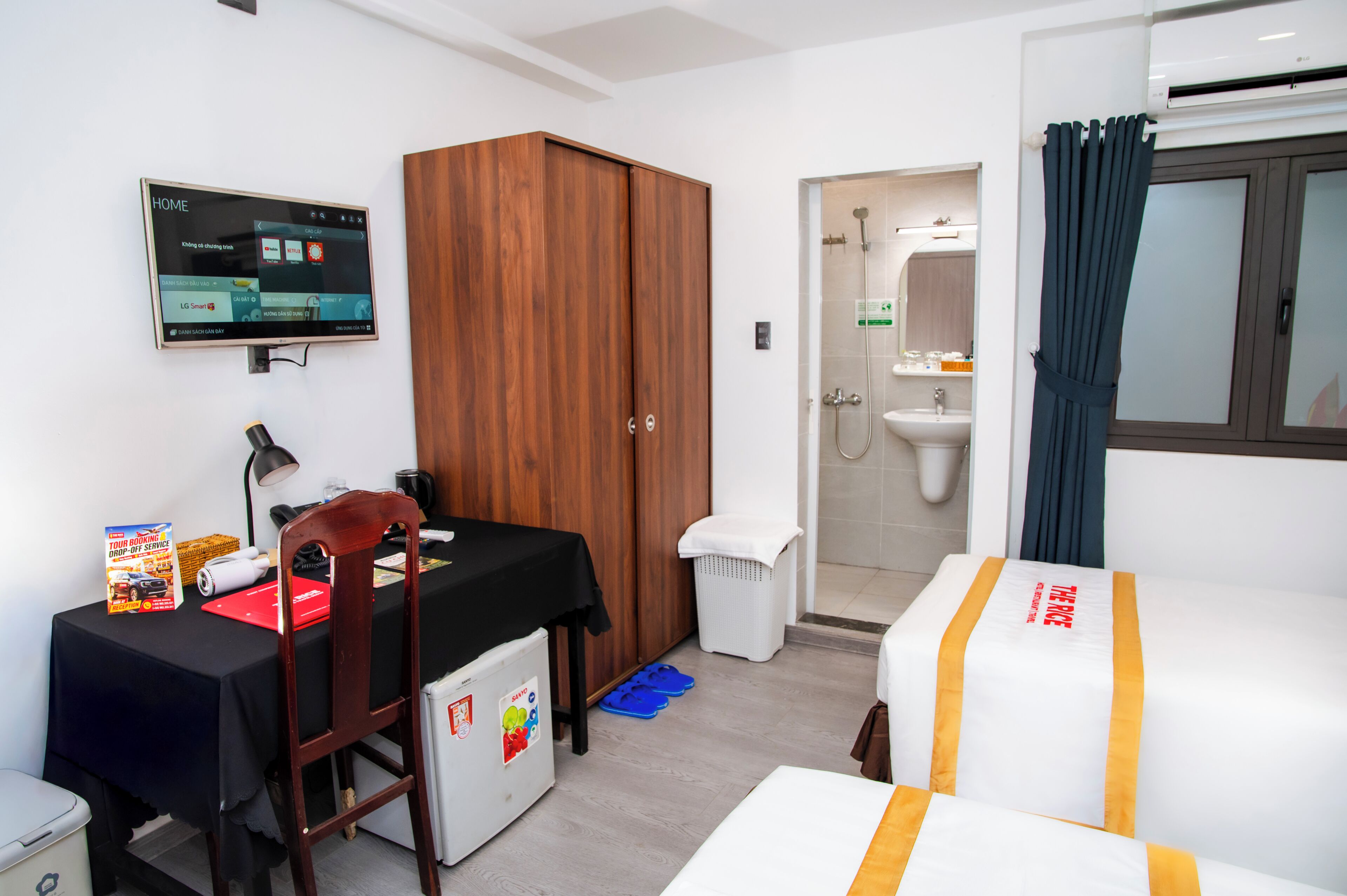 Hotelkamer met een bed, bureau met computer, kledingkast, badkamer met wastafel en douche, en een aan de muur bevestigde televisie.